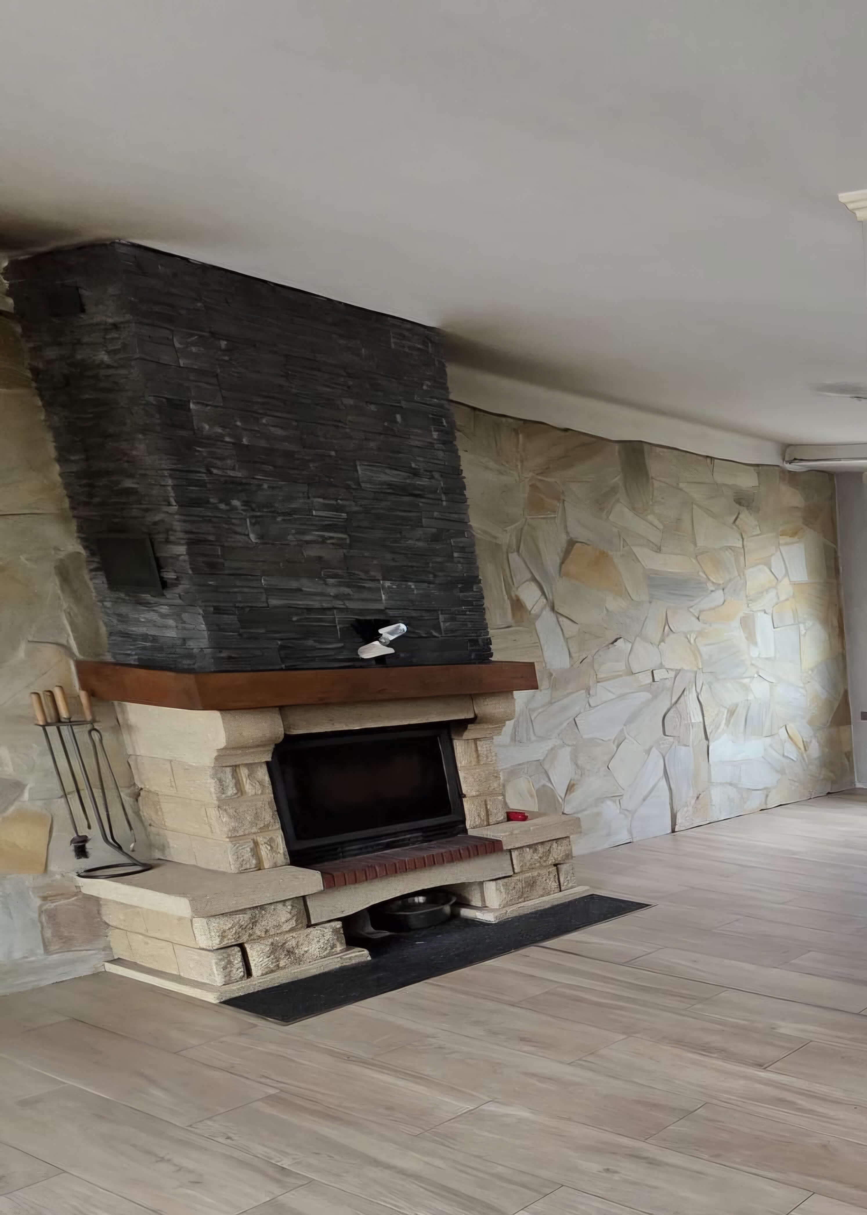 La cheminée d'origine : socle en pierre reconstituée et hotte en parement ardoise, jusqu'au plafond.